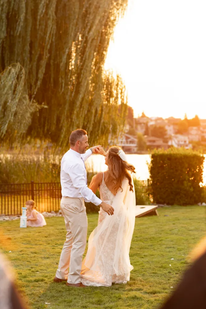 Groom twirling the bride in golden sunset light on the lawn by the lake