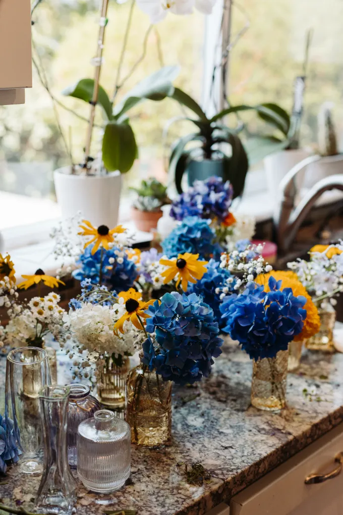 Blue hydrangea, black-eyed Susan, and baby's breath arrangements in small glass vases on a kitchen counter