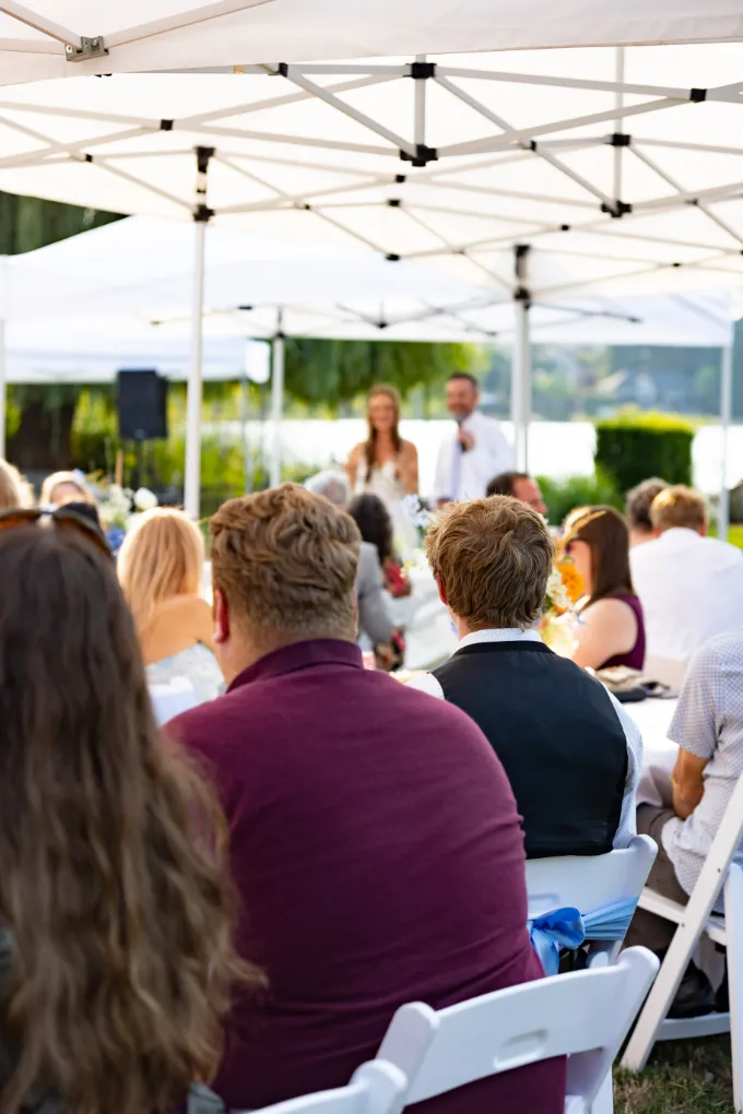 Bride and groom giving a toast under a white tent as seated guests look on