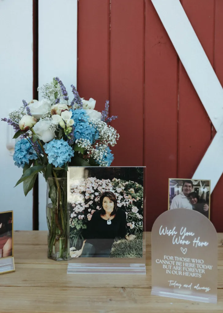 Wish You Were Here memorial table with framed photos and a hydrangea and lavender bouquet in front of a red barn door