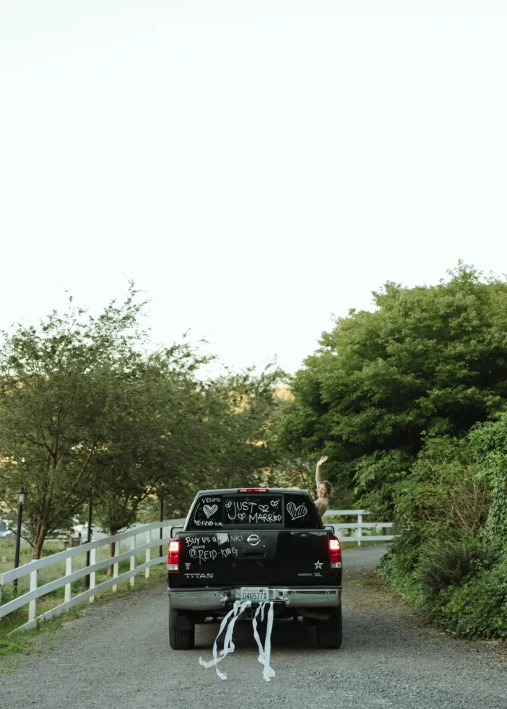 Just-married pickup truck with ribbons trailing behind as the bride waves from the window