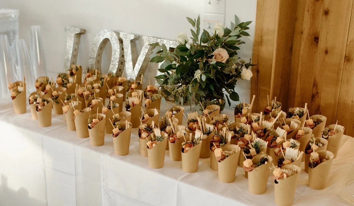 Rustic favor table with a LOVE sign and rows of wrapped appetizer cones