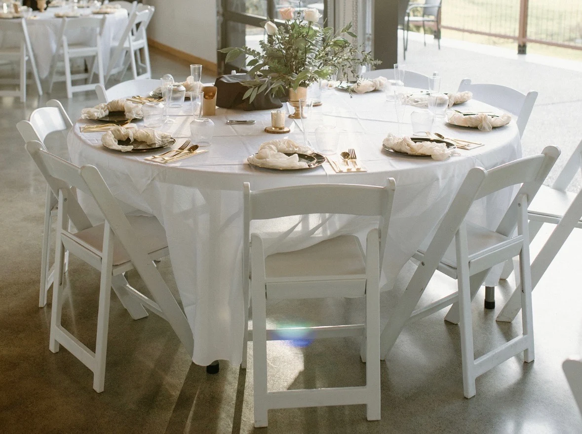 Reception table set with white linens, gold flatware, and a greenery centerpiece