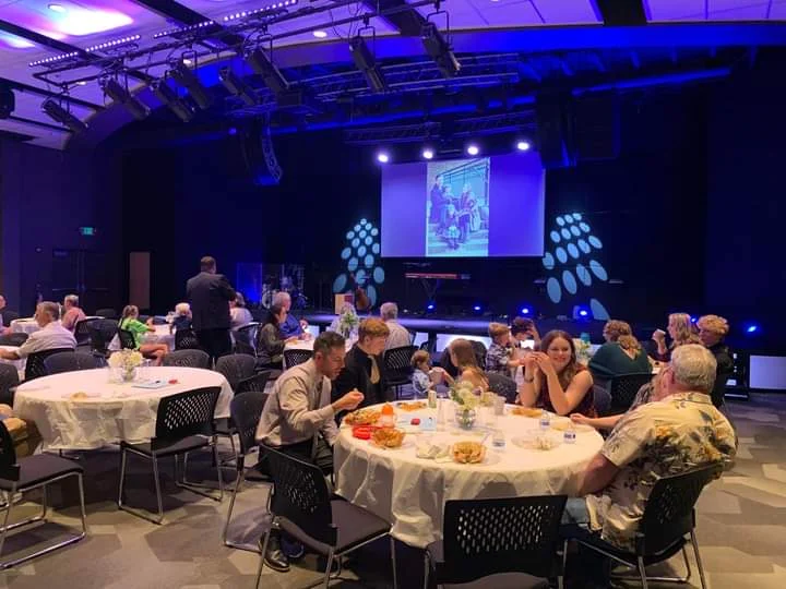 Guests seated at round tables during an indoor evening event with stage lighting