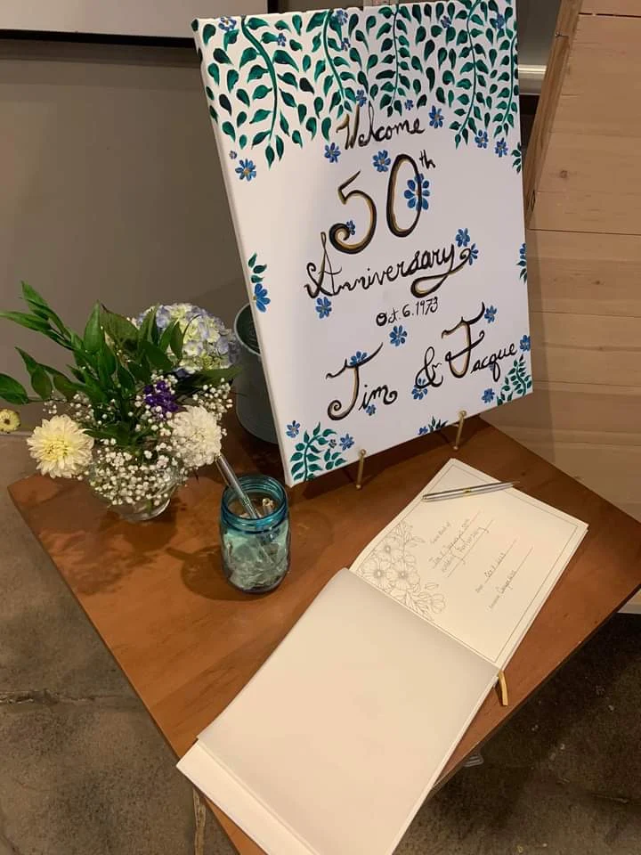 Anniversary celebration sign and guestbook table with fresh flowers