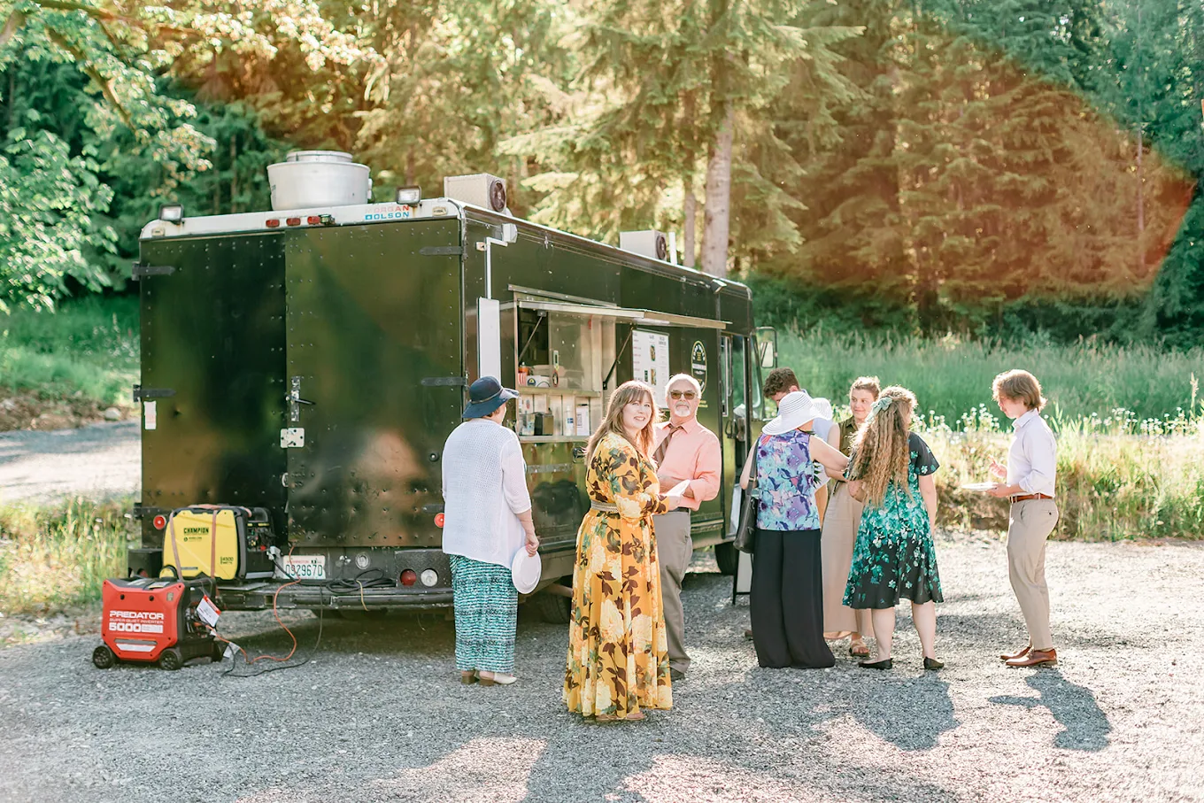 Guests gathered outdoors around a catering food truck in a wooded setting