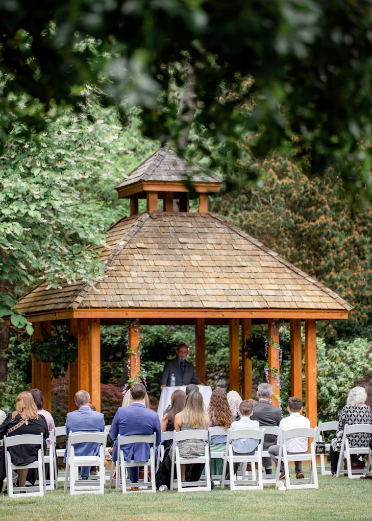Outdoor wedding ceremony beneath a wooden gazebo surrounded by trees