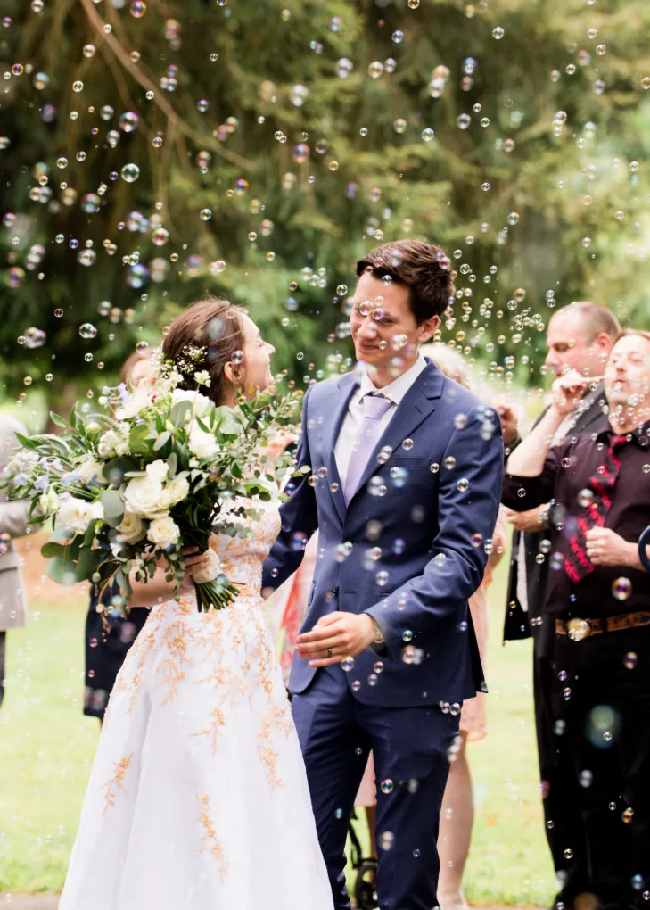 Bride and groom smiling at each other in a shower of bubbles during an outdoor send-off